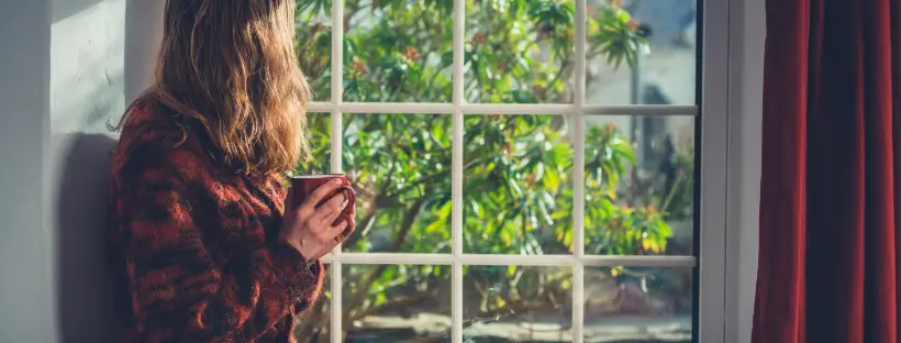 Person holding a mug and looking out a window, symbolizing ideal reflective moments for meditation during nervous system recovery