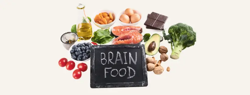 A spread of whole, nutrient-dense foods including salmon, avocado, walnuts, blueberries, and broccoli surrounding a chalkboard with ‘BRAIN FOOD’ written on it—symbolizing real food for brain health and balance.