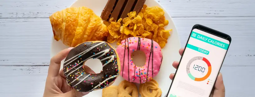 A plate of hyperpalatable foods including donuts, croissants, and cornflakes, juxtaposed with a calorie-counting app, highlighting the disconnect between calorie tracking and real food quality.