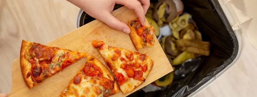 Discarded pizza slices being thrown into a trash bin, symbolizing the rejection of hyperpalatable foods and breaking free from engineered food addiction.