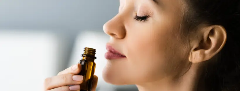 Woman smelling essential oil bottle with eyes closed, representing clean scent that calms the nervous system.