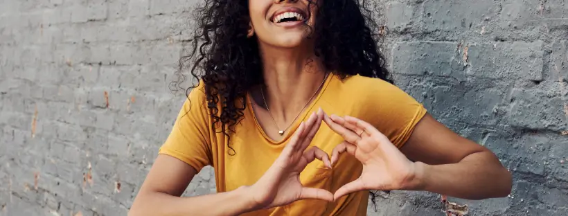 Woman smiling and forming a heart with her hands, symbolizing emotional connection and inner well-being in holistic health