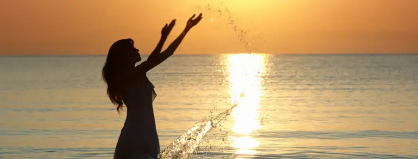 Silhouetted woman splashing water at sunset—symbolizing emotional release, balance, and the integration of holistic healing.