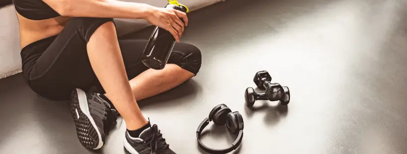 Woman resting after a workout with water bottle, weights, and headphones—representing consistent, mindful physical health practices