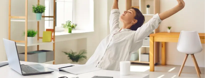 Woman stretching at her desk in a bright, minimalist home office—illustrating occupational health, mindful work habits, and how to balance career success with mindfulness.