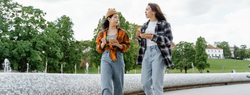 Two women walking and talking outdoors, representing authentic connection and supportive relationships in holistic social health