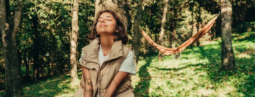 Woman sitting peacefully in a forest with eyes closed, representing spiritual wellness, inner alignment, and practices like Discursive Meditation and connecting with the 7 chakras.