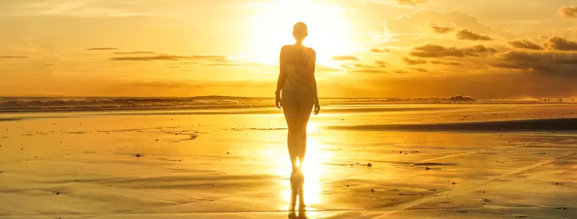 Woman walking alone on the beach at sunrise, symbolizing whole-body integration and the systems-based approach of holistic health