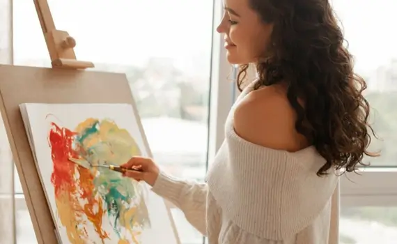 Woman painting by a sunlit window, embracing calm and creativity.