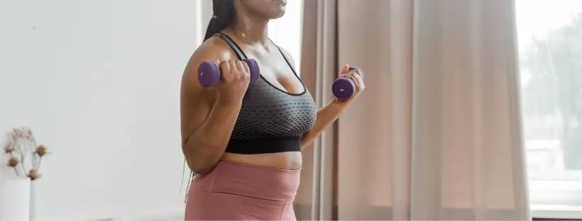 Woman lifting dumbbells during a home strength training workout, representing natural fitness and insulin balance for women over 40.