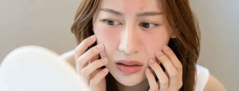 Woman with red irritated skin looking in mirror, showing common signs of sensitive skin